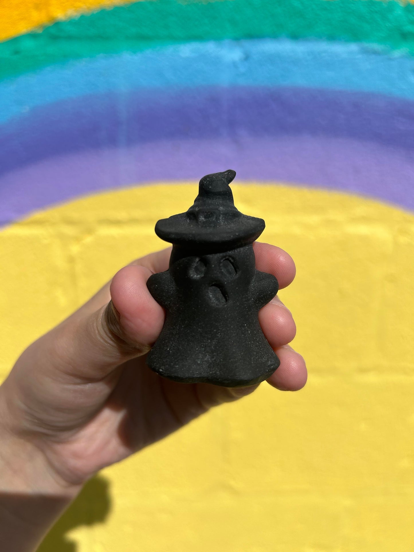 Hand holding black obsidian wizard ghost carving with colorful rainbow background