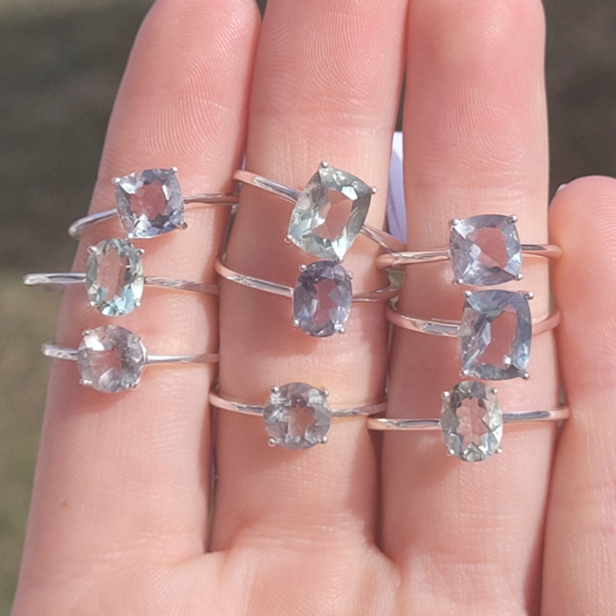 hand displaying multiple silver rings with faceted green fluorite gemstones in various shapes