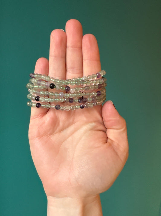 Hand holding a delicate 4 mm fluorite bracelet with natural green and purple beads for mental clarity and emotional balance