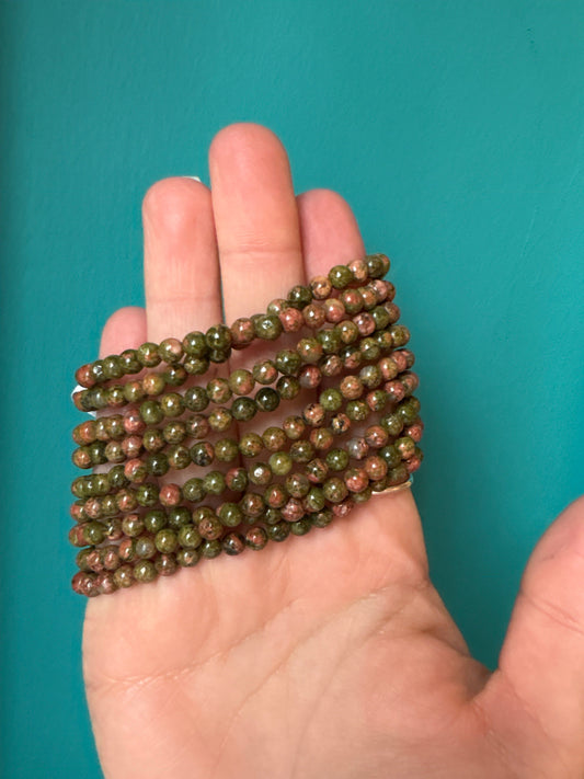 Bracelet Unakite with 4mm natural green and pink beads held in hand against blue background