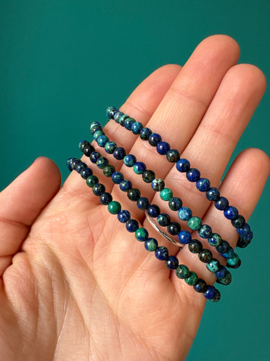 Hand holding multiple 4mm azurite malachite bead bracelets with blue and green tones