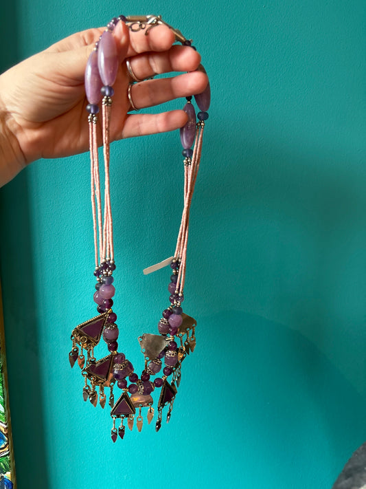 Vintage Afghanistan necklace with purple beads and intricate metal charms held against a teal background