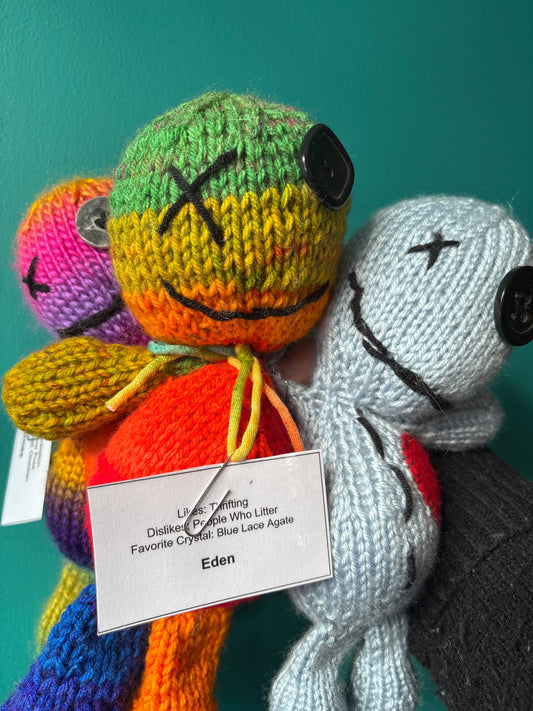 Colorful knitted emotional support voodoo dolls with unique personalities and favorite crystals, including one named Eden with a blue lace agate crystal.