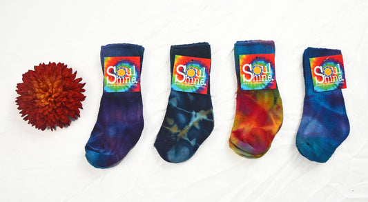 Four pairs of kids cotton dancing socks in assorted tie-dye colors with Soul Shine labels displayed next to a red flower on a white background