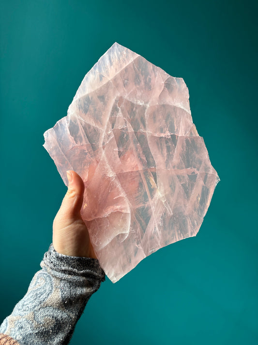 Hand holding a large translucent rose quartz slab against a teal background