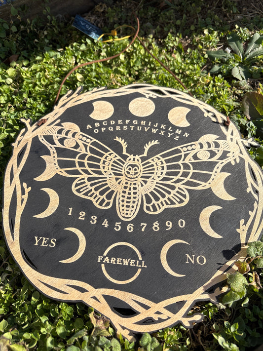 Moth Ouija Board Wall Hanging with crescent moons and alphabet design on black background outdoors on grass