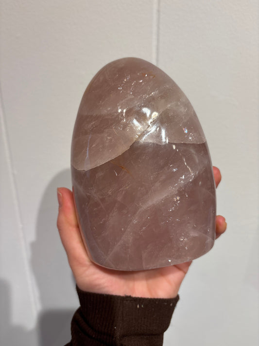 Hand holding a polished rose quartz freeform crystal stone against a plain background