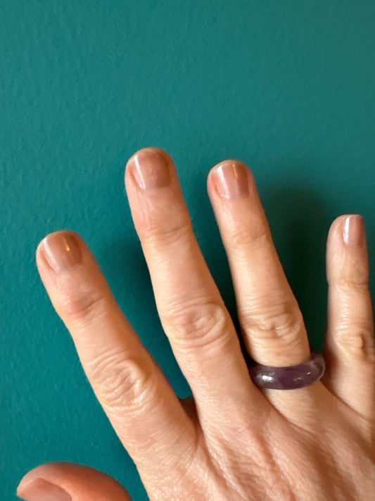 Hand wearing a polished Amethyst ring against a teal background