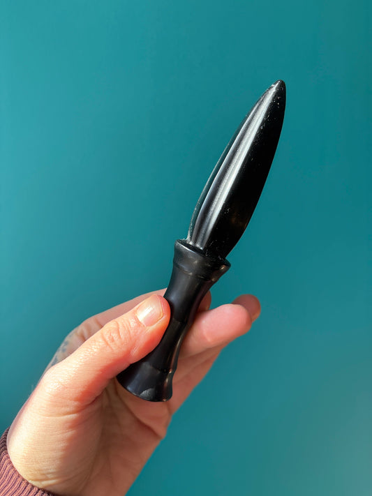 hand holding sleek black dagger obsidian against blue background