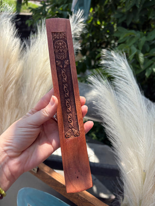 Wood incense holder with carved hamsa design held outdoors against natural background