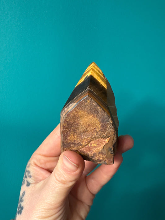Hand holding a polished Tigers Eye top point crystal against a blue background