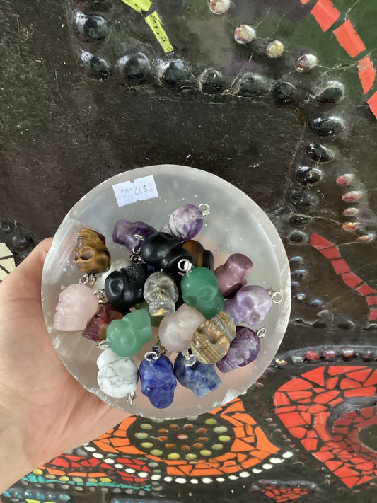 Hand holding a collection of pendant skulls made from mixed crystals in various colors and patterns