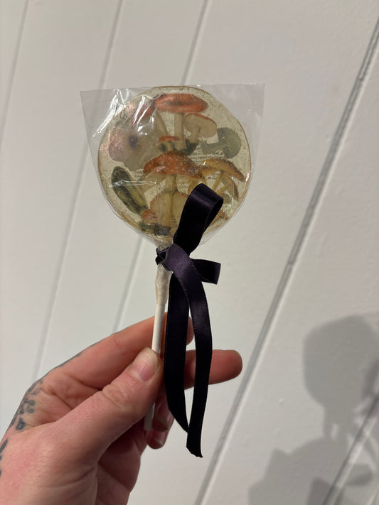 Hand holding a transparent mushroom lollipop with a black ribbon bow against a white background