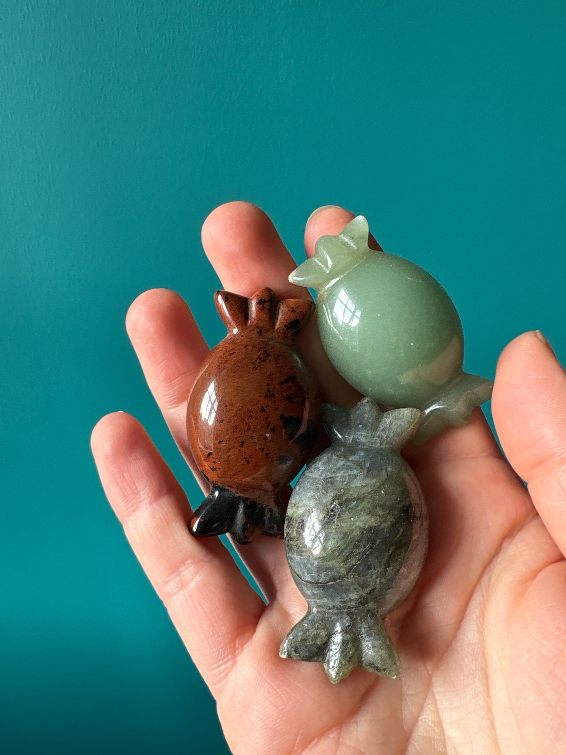 Hand holding three crystal candy carvings in green, brown, and gray stones against a teal background