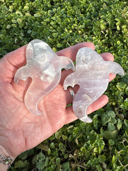 Hand holding two ghost-shaped flat Lavender Fluorite crystals on green foliage background Ghost Lavender Fluorite gemstones
