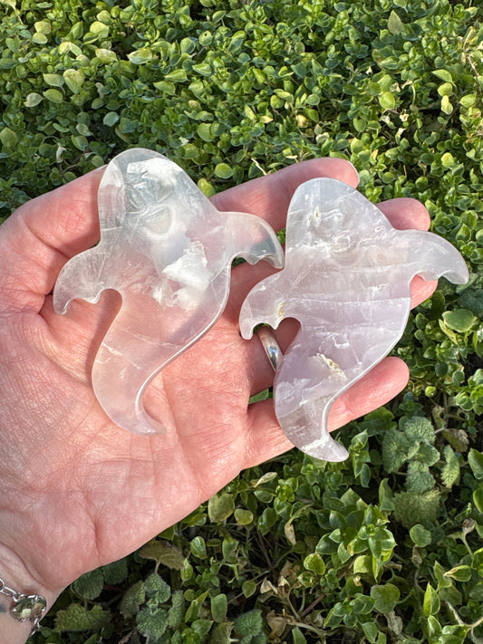 Hand holding two ghost-shaped flat Lavender Fluorite crystals on green foliage background Ghost Lavender Fluorite gemstones