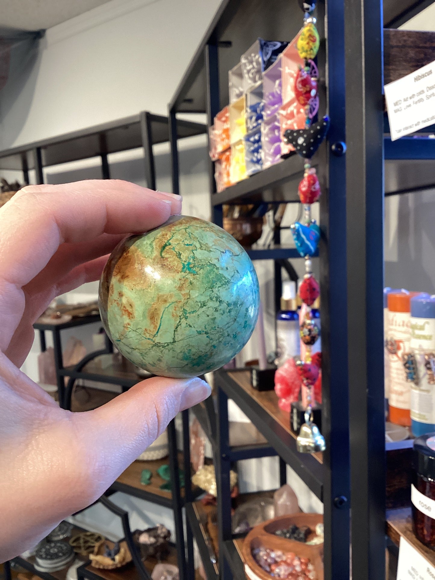 Hand holding a turquoise sphere in a store with colorful hanging decorations and shelves in the background