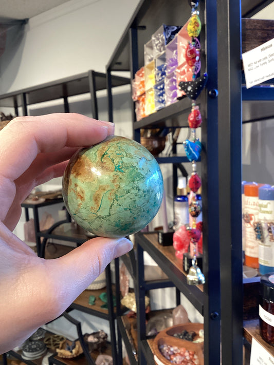 Hand holding a turquoise sphere in a store with colorful hanging decorations and shelves in the background