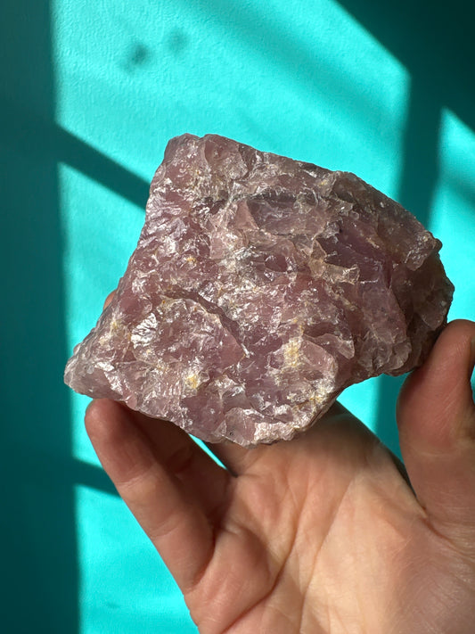 Hand holding a raw guava quartz crystal with a turquoise background