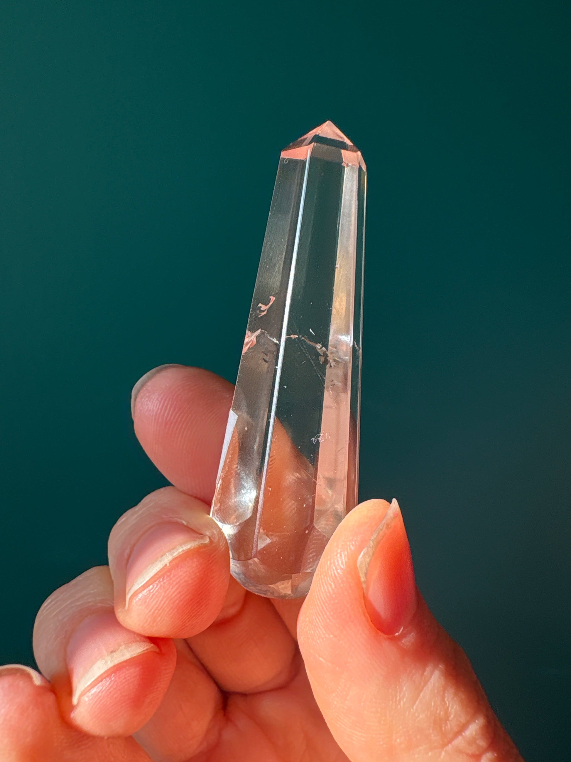 Clear Quartz 6 Facets Massager held between fingers against green background