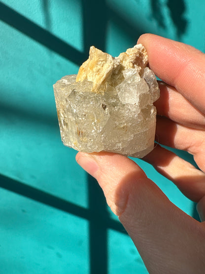 Hand holding raw topaz gemstone with natural rough texture against turquoise background