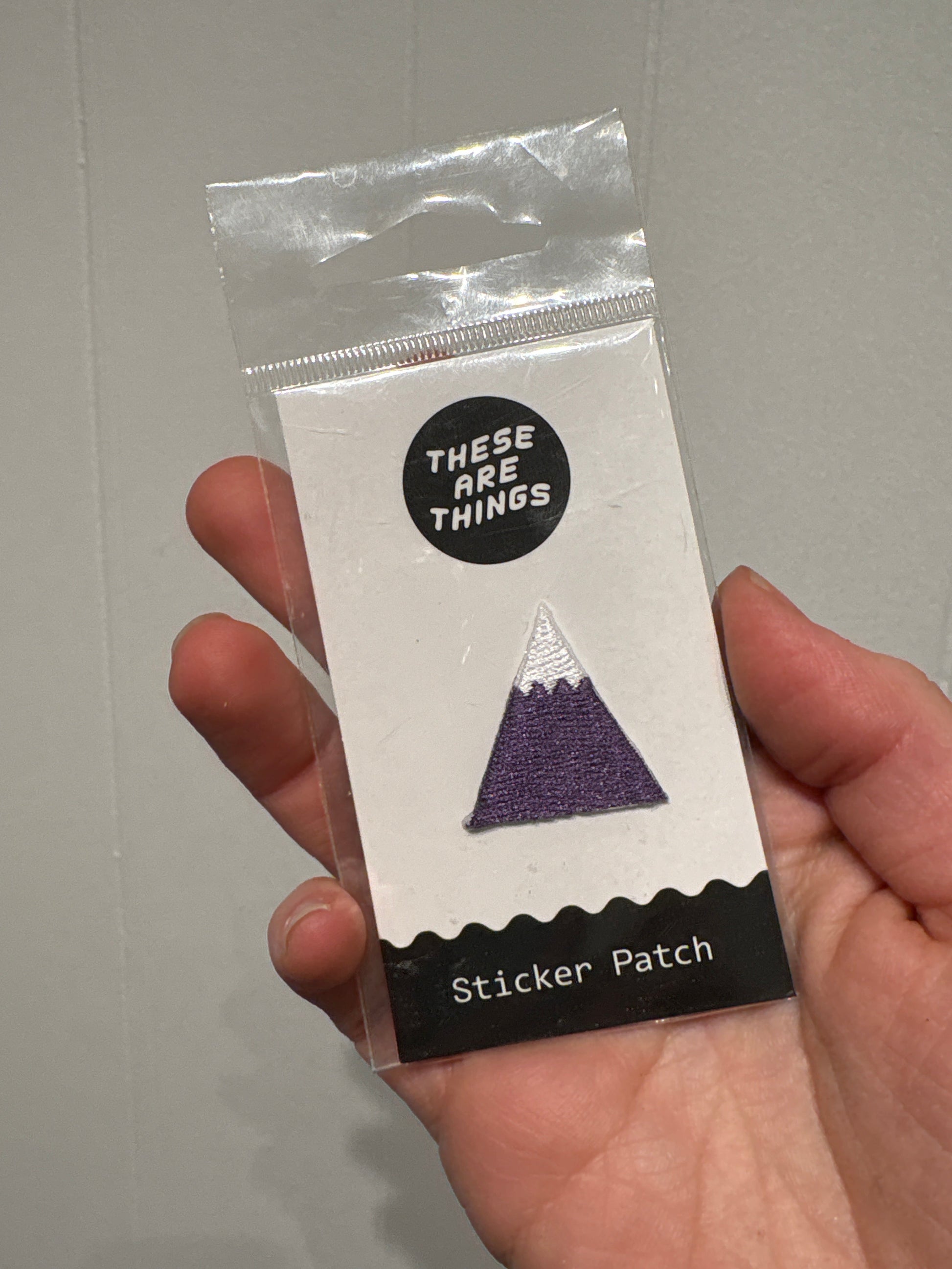 Hand holding packaged mountain sticker patch with purple and white design labeled "Sticker Patch"