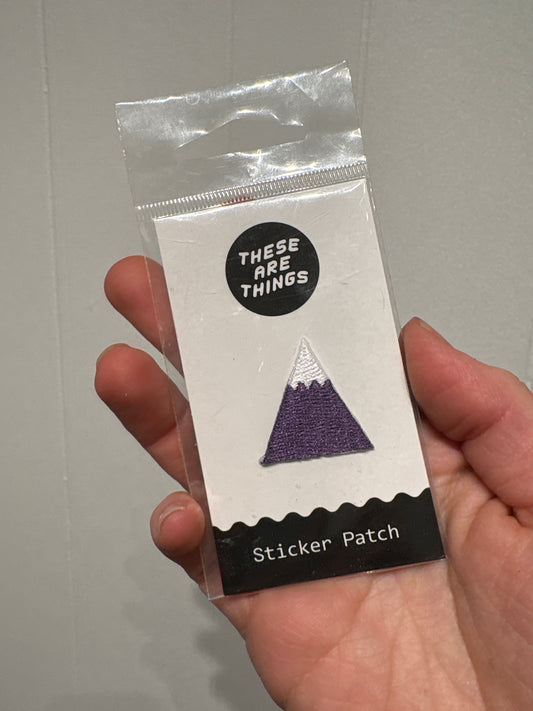 Hand holding packaged mountain sticker patch with purple and white design labeled "Sticker Patch"