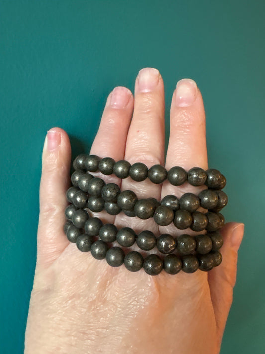 Hand wearing multiple strands of 8mm genuine pyrite bead bracelet against teal background