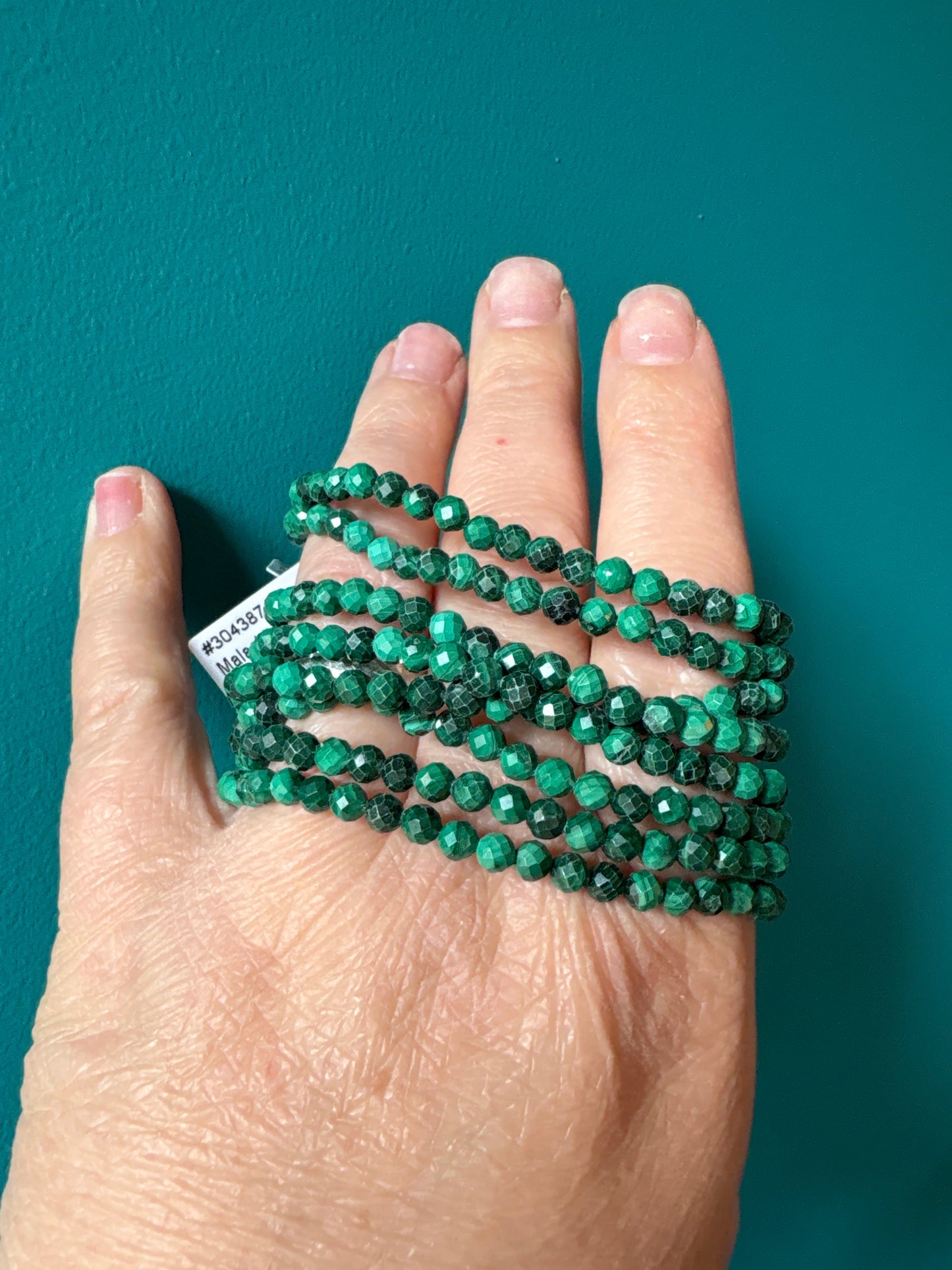 green faceted 4mm Malachite bracelet beads on hand against teal background