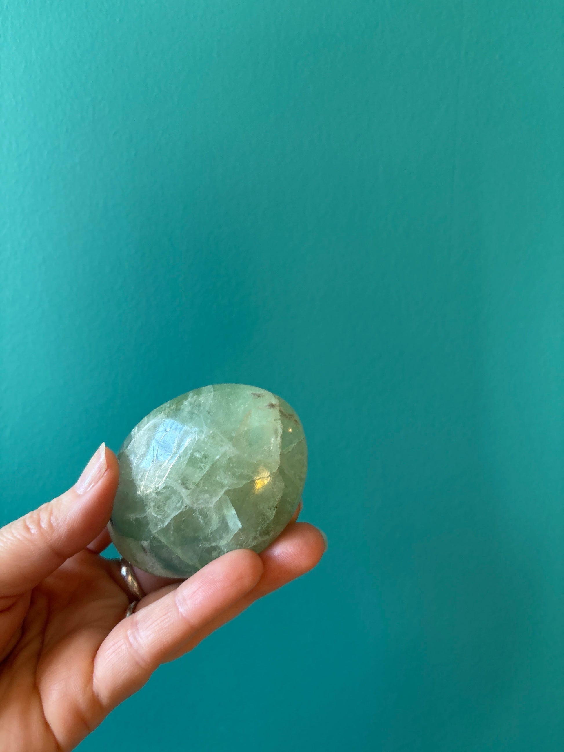 Hand holding a green Fluorite palm stone promoting mental clarity and focus against teal background
