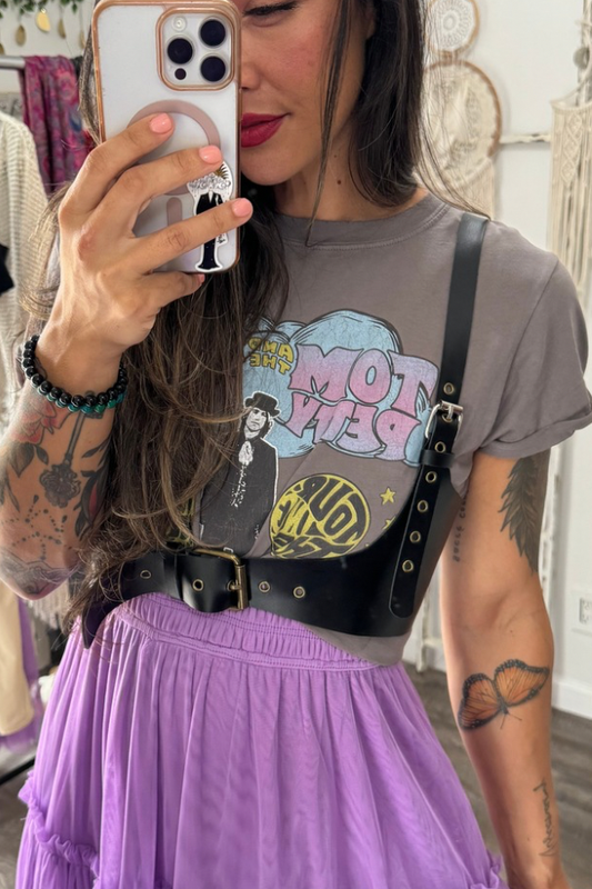 Black leather harness belt with antique bronze hardware worn over graphic t-shirt and purple skirt