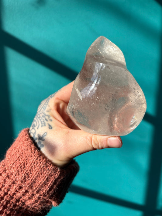 Hand holding a flame-shaped smokey quartz crystal against a teal background