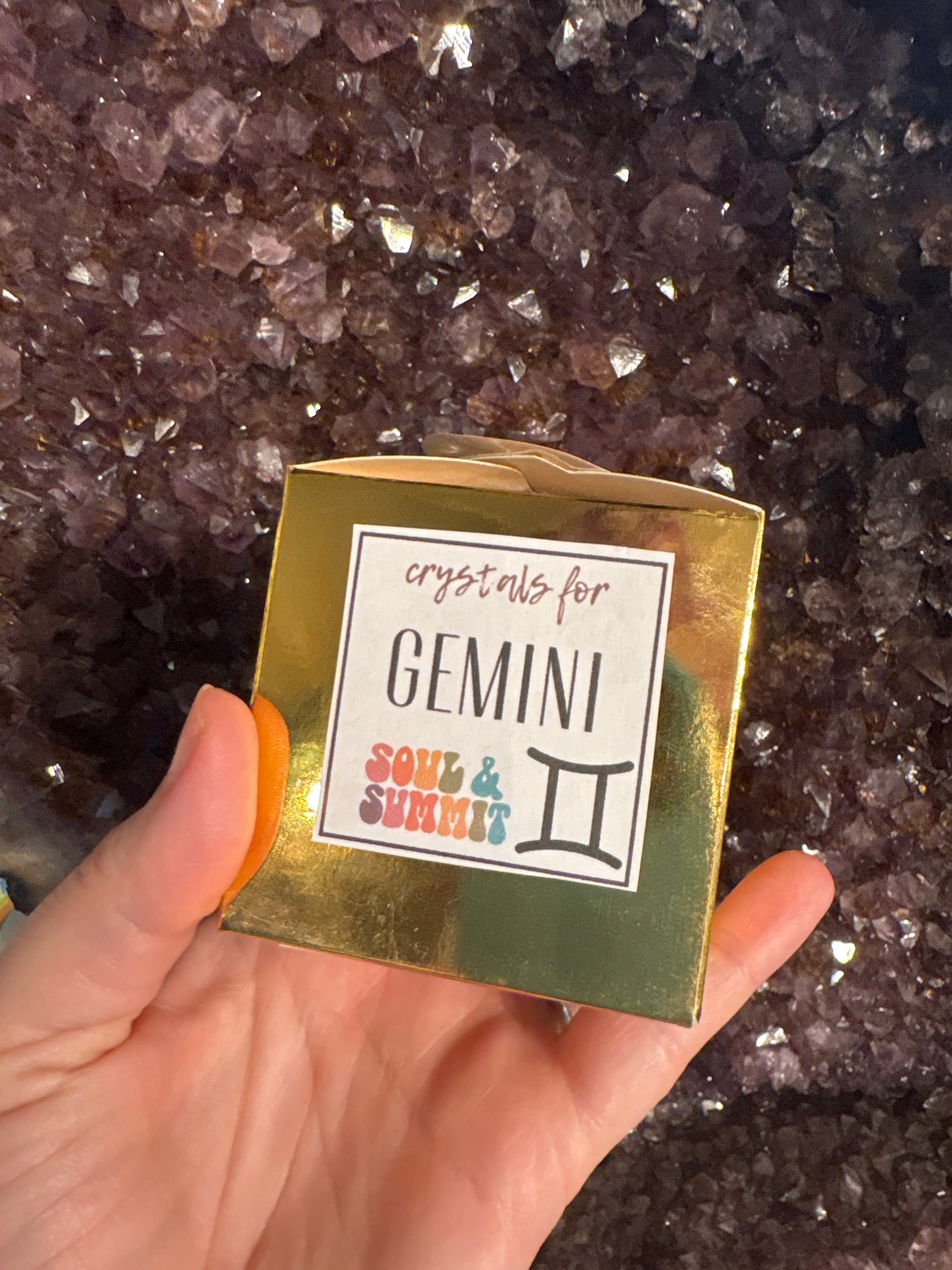 Gemini Crystal Box zodiac gift with crystals in gold packaging held over amethyst background