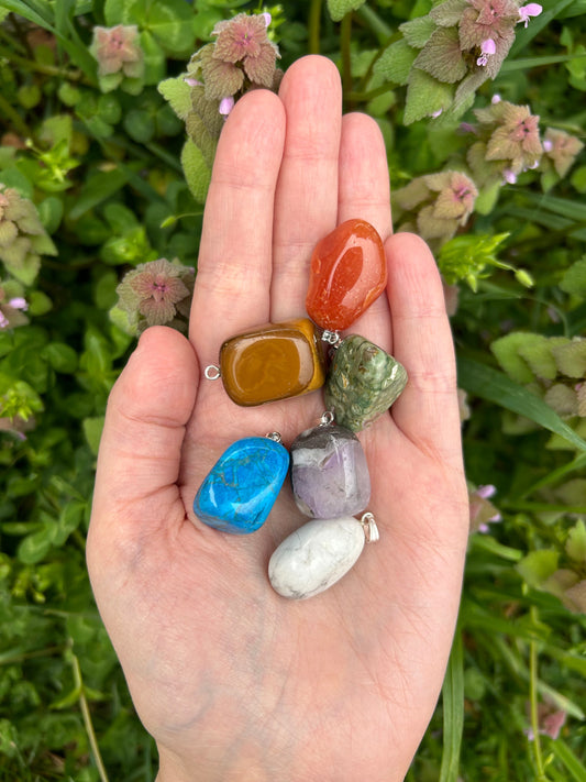 Hand holding mixed crystal tumble pendants in various colors with green foliage background