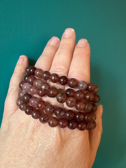 Bracelet Strawberry Quartz 8mm beads on hand against teal background, polished round stones, spiritual jewelry accessory