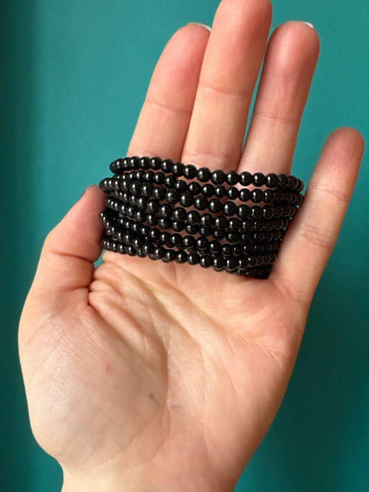 Hand holding multiple strands of 4mm black tourmaline bead bracelets on teal background