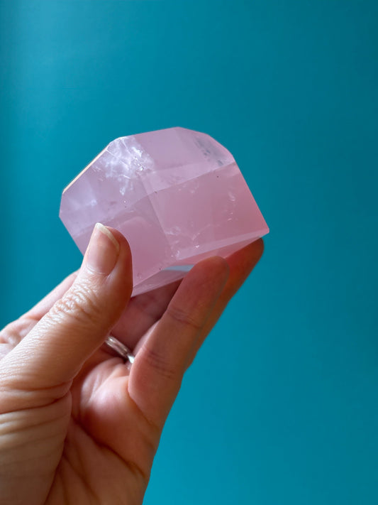 Freeform Geometric Rose Quartz crystal held in hand with a teal background promoting healing and self-love