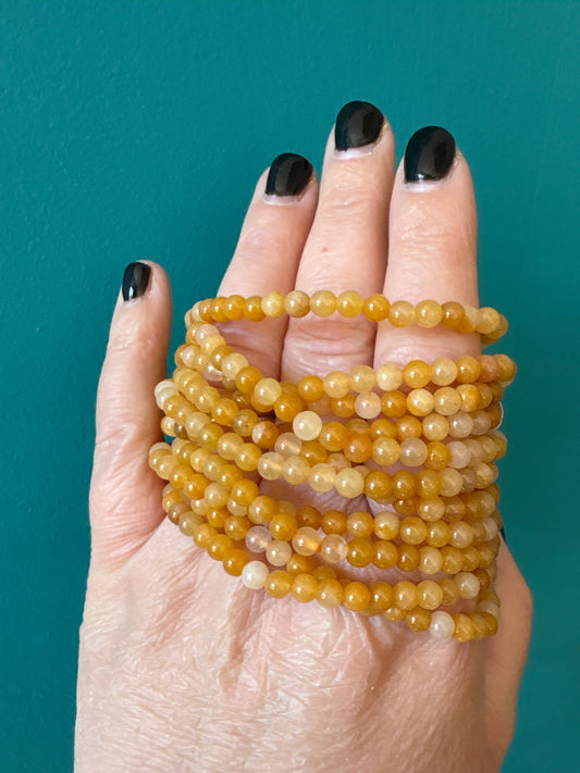 Yellow Jade 4mm bead bracelet wrapped around hand with black nail polish on teal background