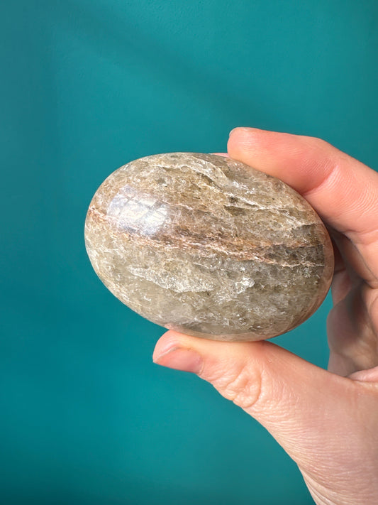 Hand holding a polished Smokey Quartz Palm Stone against a teal background