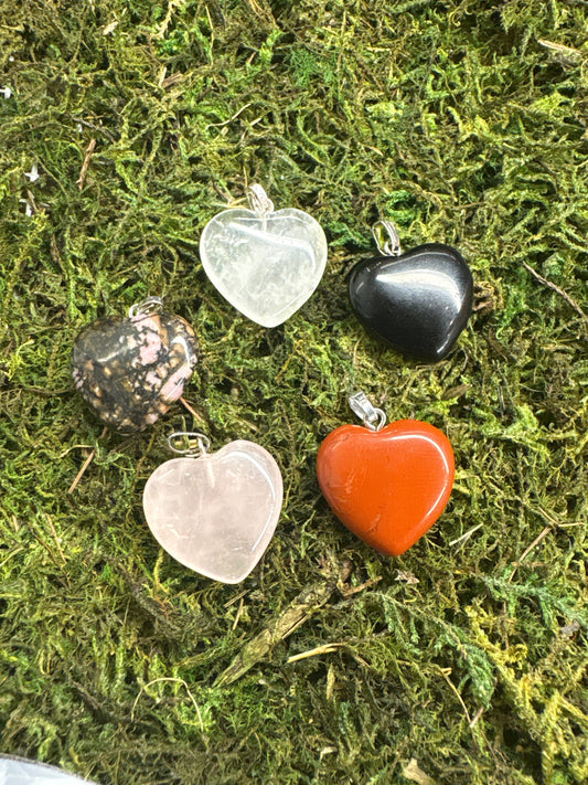 Collection of crystal heart pendants in various colors displayed on green moss background