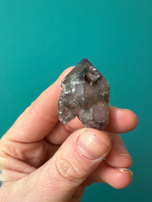 hand holding raw Shangaan amethyst stone with purple hues against teal background