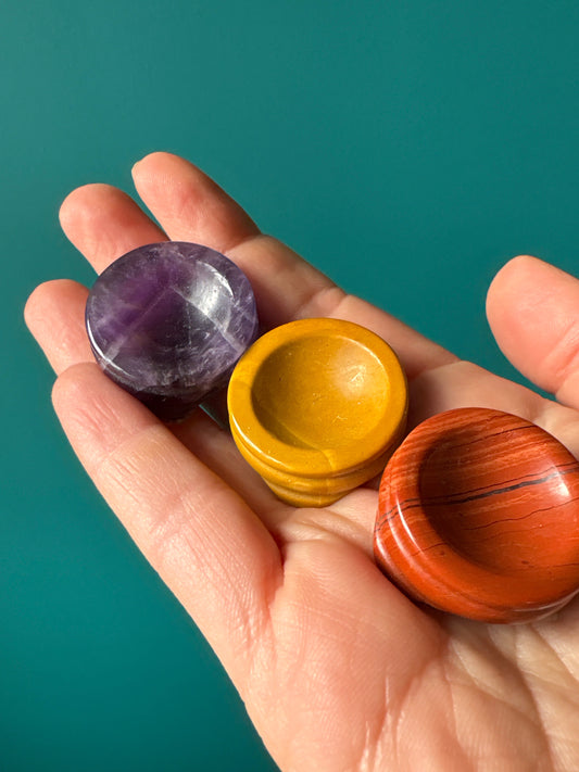 Hand holding three crystal sphere stands in purple, yellow, and red colors against teal background