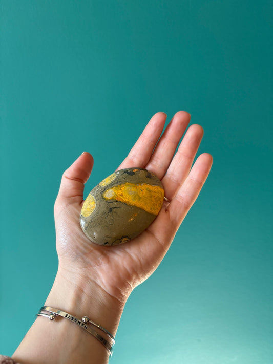 hand holding Bumble Bee Jasper Palm Stone with yellow and gray patterns against teal background
