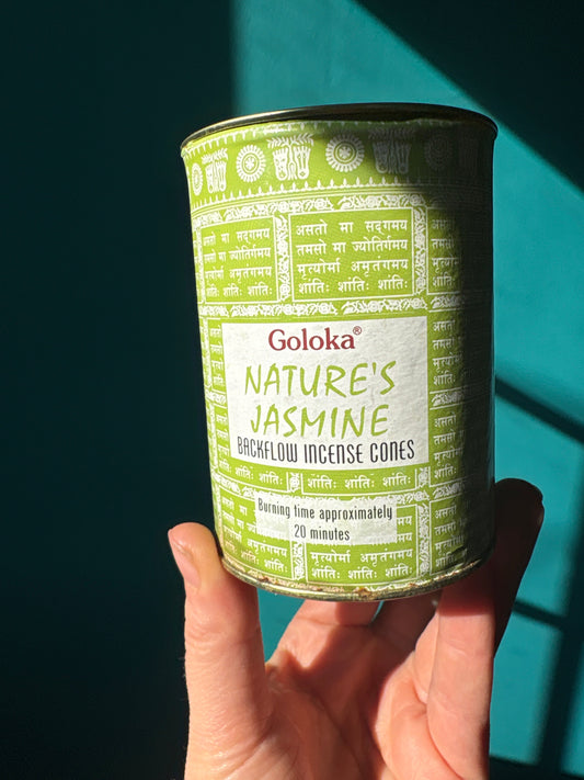 Goloka Nature's Jasmine Backflow Incense Cones container held against turquoise background
