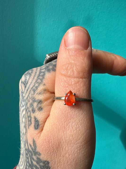 Ring Mexican Fire Opal with pear-shaped vibrant orange gemstone on silver band worn on finger against teal background