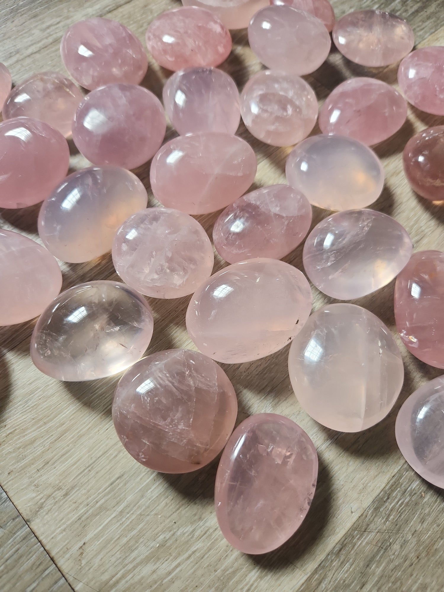 Smooth polished palm stone rose quartz crystals in soft pink hues arranged on a wooden surface for self-love and harmony