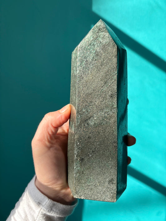 Hand holding a polished green aventurine tower crystal against a blue background