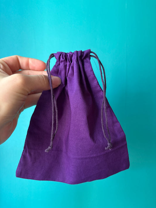 Hand holding a purple cotton chakra pouch with drawstrings against a blue background