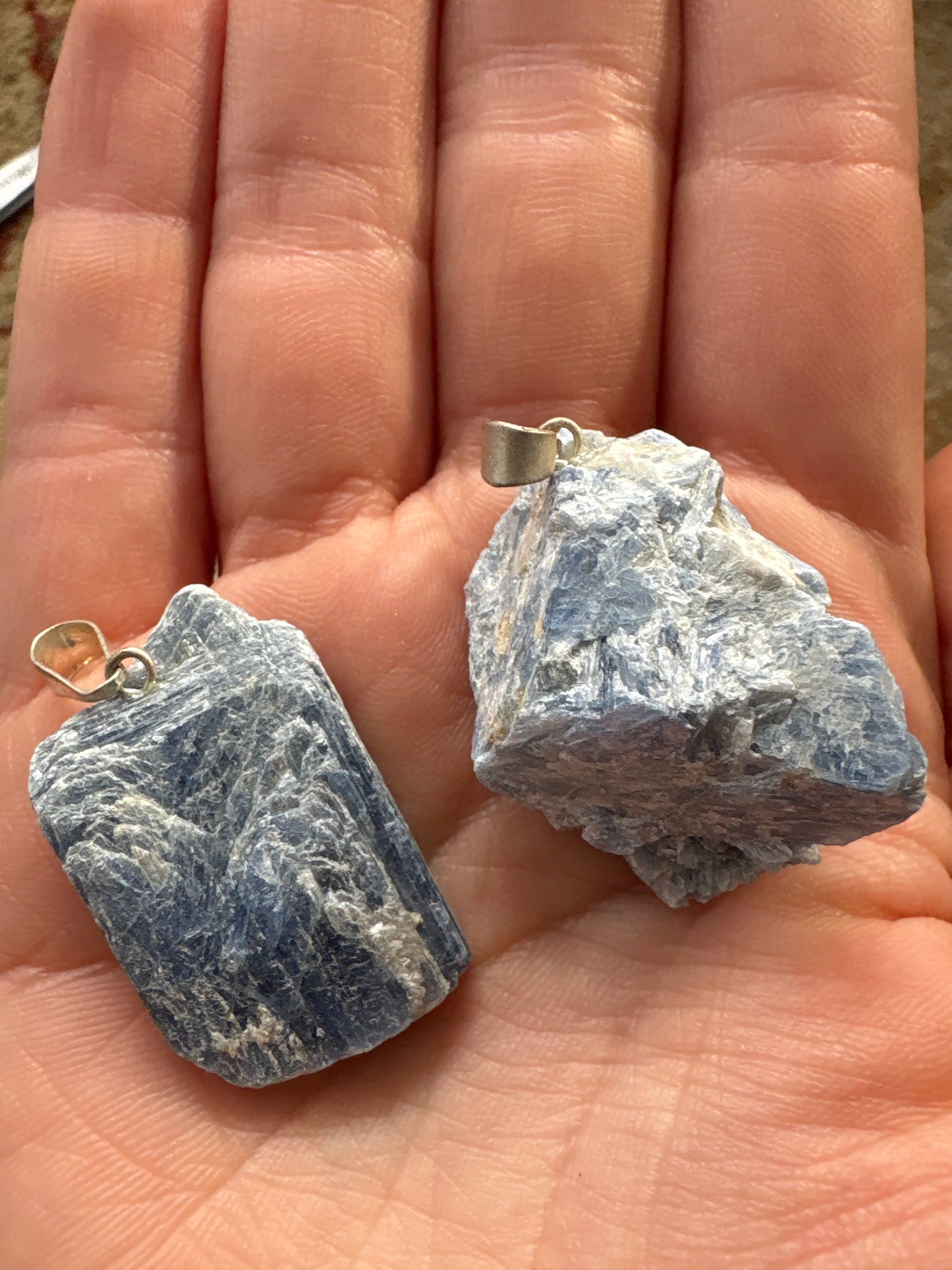 Hand holding two raw blue kyanite pendants with silver bails showcasing natural stone texture and color
