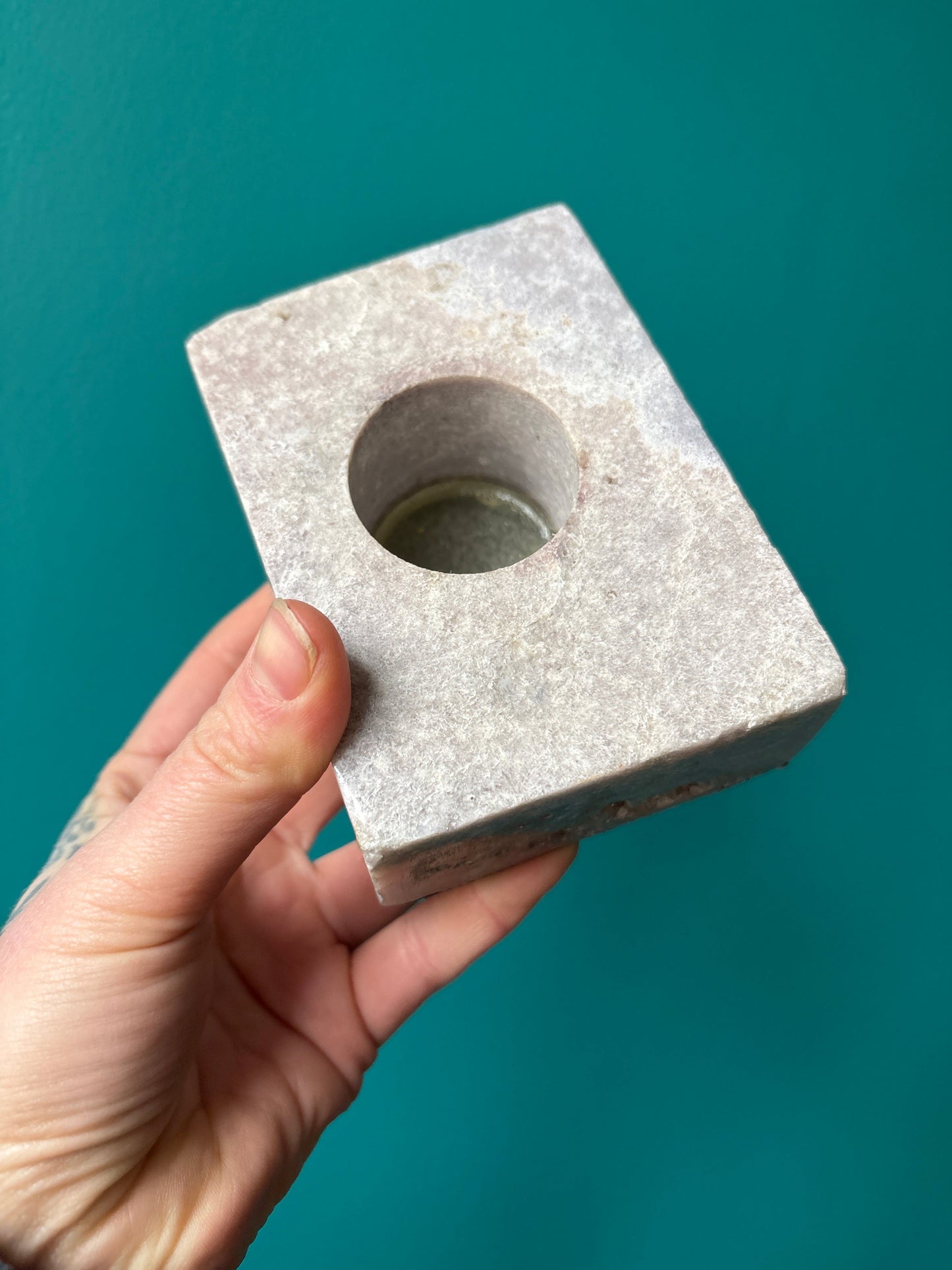 Hand holding a square pink amethyst candle holder with a round center opening against a teal background